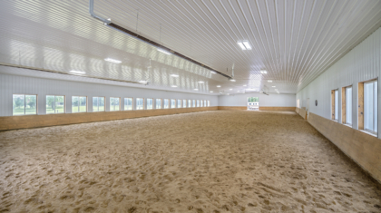 A panoramic view of a large indoor riding arena with windows from Miller Diversified's Mockingbird Barn Commercial Construction Project